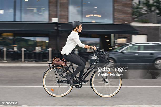 full length of businesswoman riding bicycle on city street - business woman side stockfoto's en -beelden
