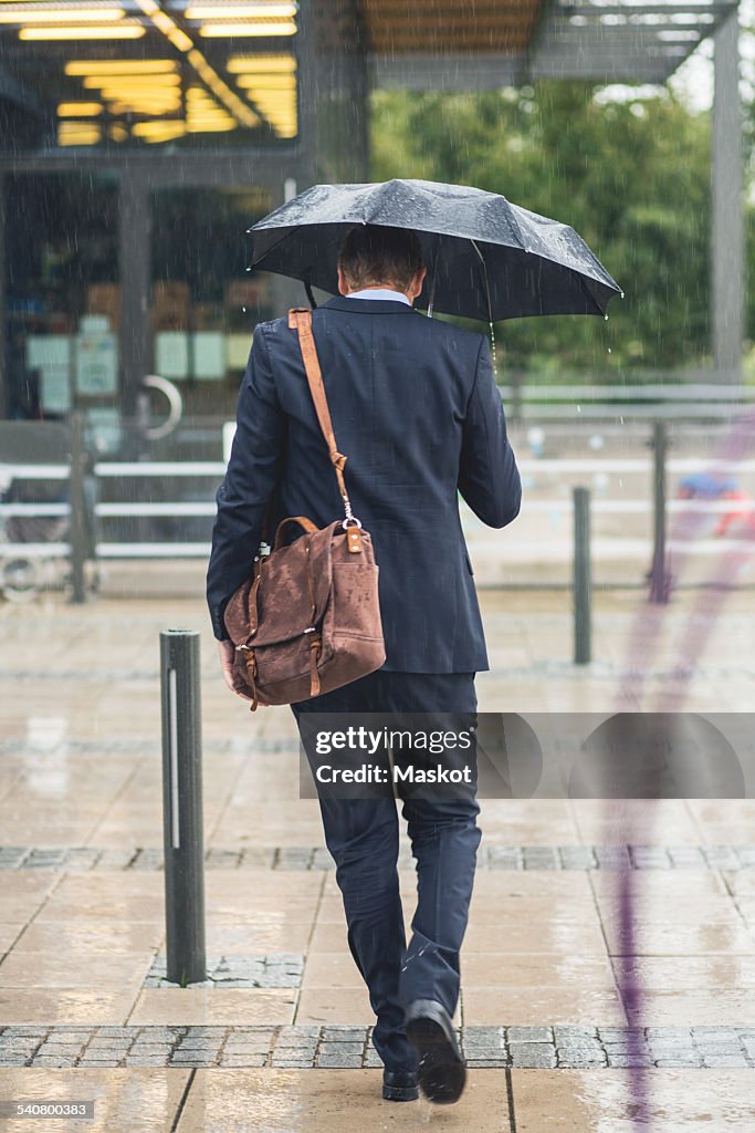 Full length rear view of businessman walking on sidewalk during rainy season