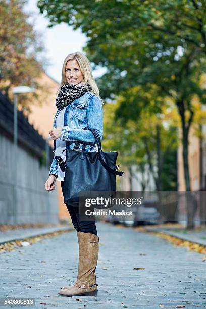 full length portrait of mid adult woman standing on street - white handbag stockfoto's en -beelden