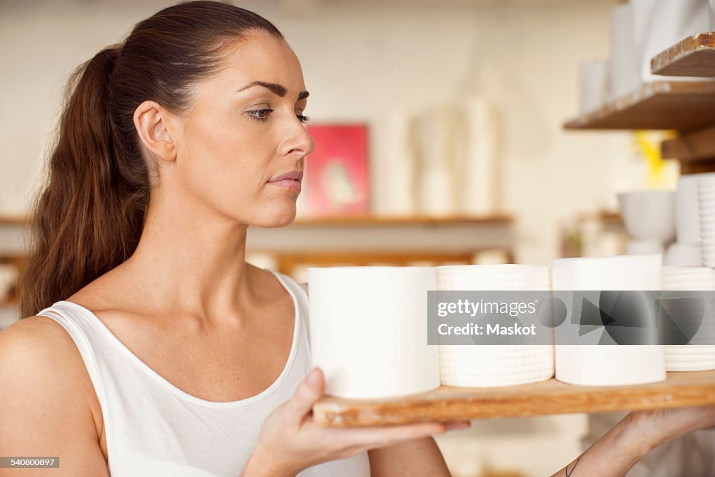 Female worker arranging craft products in crockery workshop