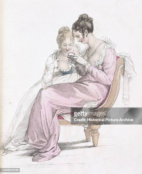 Two ladies dressed in early 19th century low-necked, Empire line, evening dresses admire a trinket.