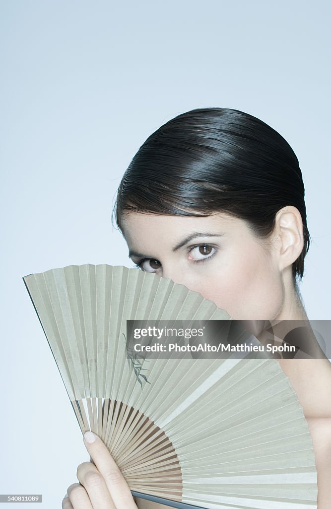 Woman holding fan in front of her face, portrait