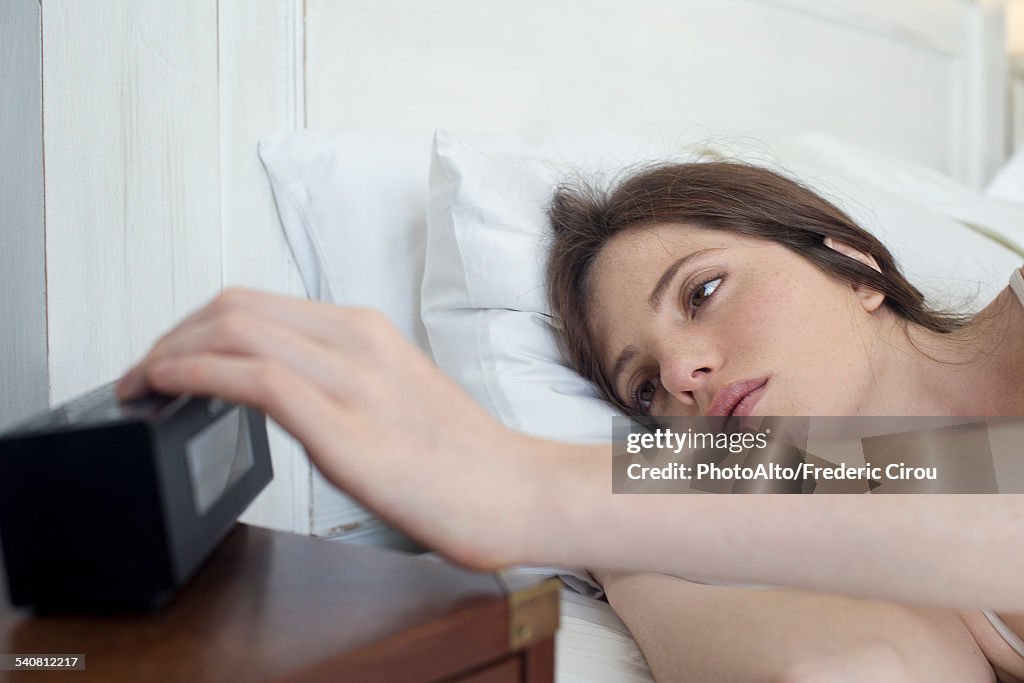 Woman in bed pressing alarm clock snooze button