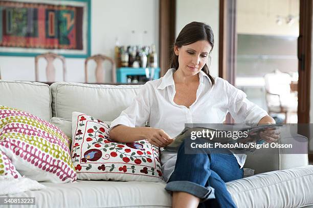 woman sitting on sofa reading magazine - mujer revista fotografías e imágenes de stock