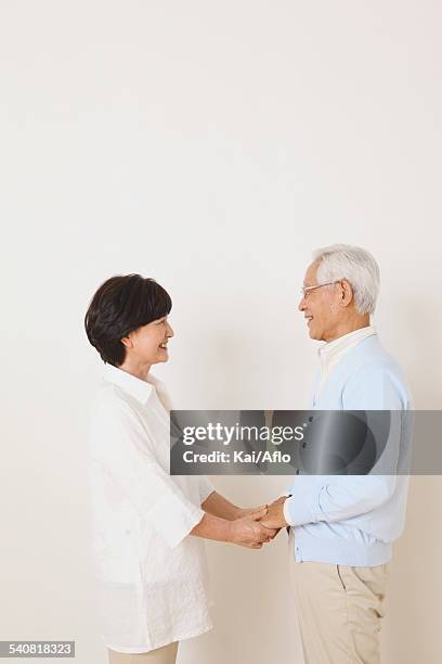senior adult japanese couple against white wall - man and woman holding hands profile stockfoto's en -beelden