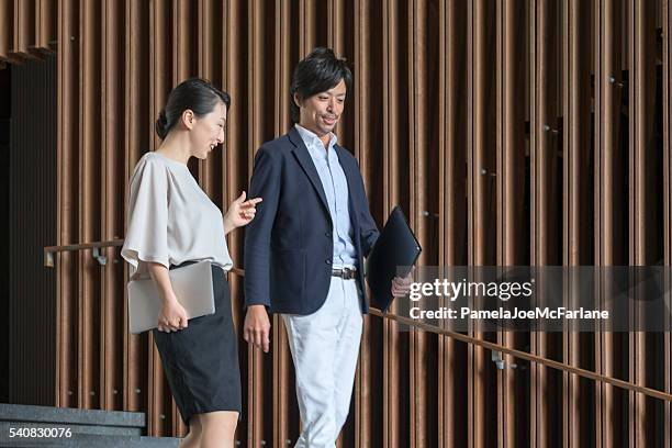 businesswoman, businessman having conversation while holding laptop, office lobby - businessmen casual not phone walking stock pictures, royalty-free photos & images