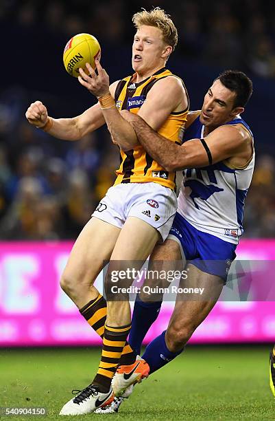 James Sicily of the Hawks handballs whilst being tackled by Michael Firrito of the Kangaroos during the round 13 AFL match between the North...