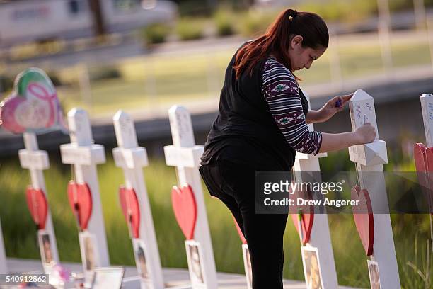 Woman writes a note on a cross at a memorial with wooden crosses for each of the 49 victims of the Pulse Nightclub, next to the Orlando Regional...