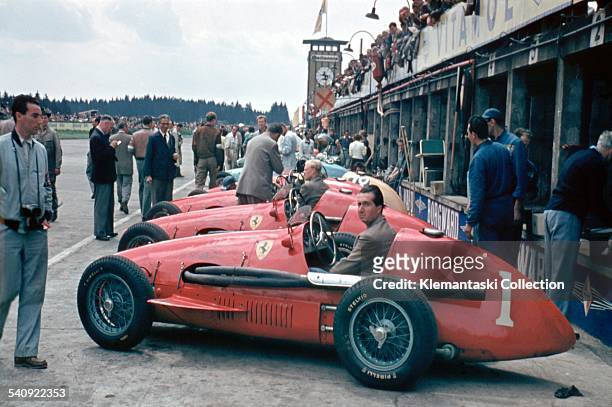 The German Grand Prix; Nürburgring, August 2, 1953. World Champion Alberto Ascari sits in his Ferrari 500/F2 in front of the pits with Mike Hawthorn...
