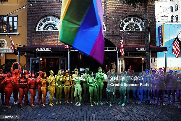 Dozens of people stand outside of a bar while painted in the colors of the rainbow flag to show their solidarity with the LGBT community following...