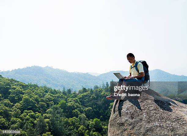 asian male hiker using laptop on rock - outdoor guy sitting on a rock stockfoto's en -beelden