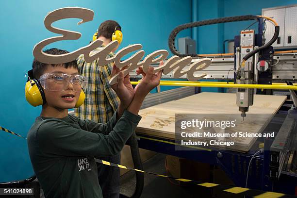 Student holds up the result of a computer-aided design and fabrication project, the name 'Eugene' cut in wood by a 'ShopBot' during a summer school...