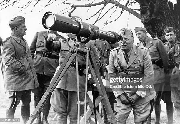 Italian dictator Benito Mussolini assesses the terrain through a telescope behind the front lines during Italy's campaign against Greece. Count Ugo...