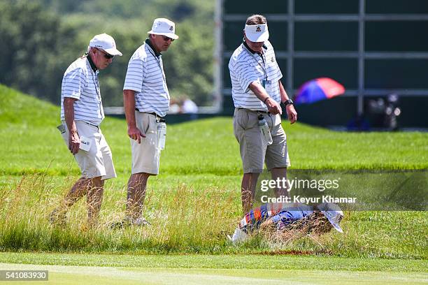 Hideto Tanihara of Japan looks for his ball in a hazard / ditch on the 18th hole fairway during the continuation of the second round of the U.S. Open...