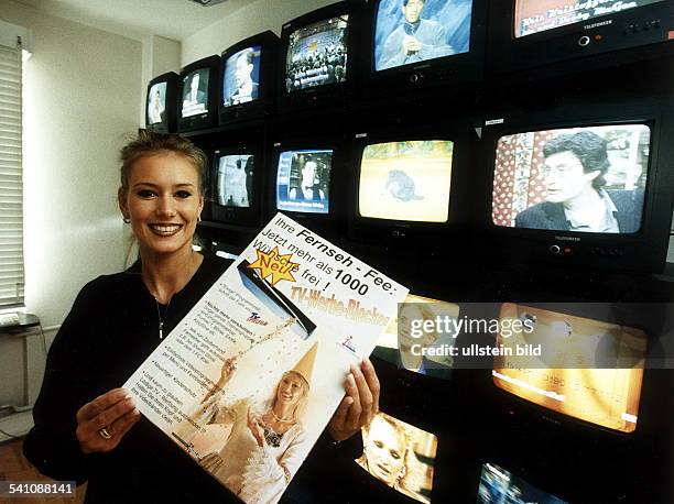 Unternehmerin, D- Chefin der TC-Unterhaltungselektronik AG Koblenzsitzt vor einer Wand mit Fernsehmonitoren mit Werbeplakat für die sogenannte...