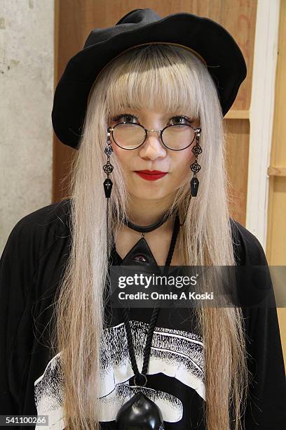 Hitomi is wearing an M:E gothic shirt, an oversized black Kewpie Doll necklace, Paris Miki eyeglasses, a CA4LA hat, a clear pvc wrist cuff, a...