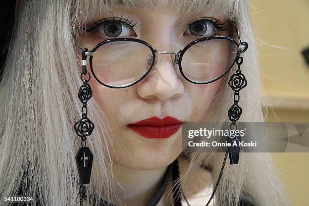 Hitomi is wearing an M:E gothic shirt, an oversized black Kewpie Doll necklace, Paris Miki eyeglasses, a CA4LA hat, a clear pvc wrist cuff, a...