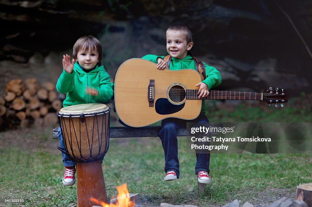 Playing Instruments In Fire Two Cute Boys Playing On Musical Instruments Around A Camp Fire High ...