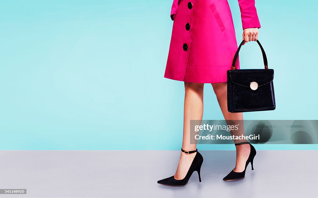 Rosa Mantel Frau mit schwarzem Leder Handtasche mit Fersen Schuhe.