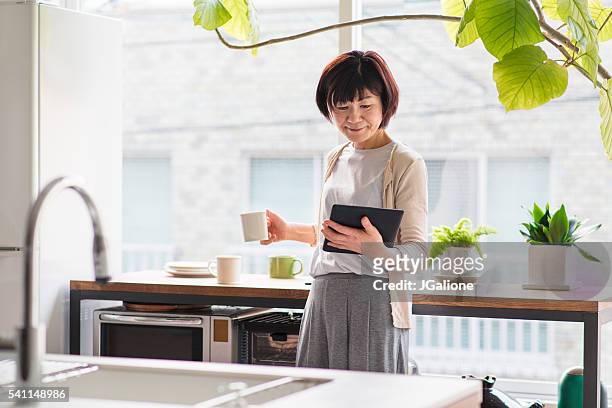 ältere frau lesung eine digitaltablett - asian woman reading stock-fotos und bilder