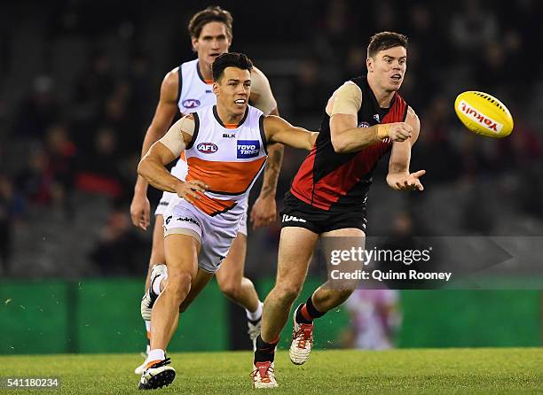 Craig Bird of the Bombers handballs whilst being tackled by Dylan Shiel of the Giants during the round 13 AFL match between the Essendon Bombers and...