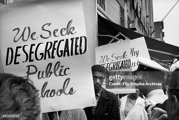 African Americans picket the sidewalks of Birmingham, Alabama for desegregated schools. A policeman confronts them for the photographers.