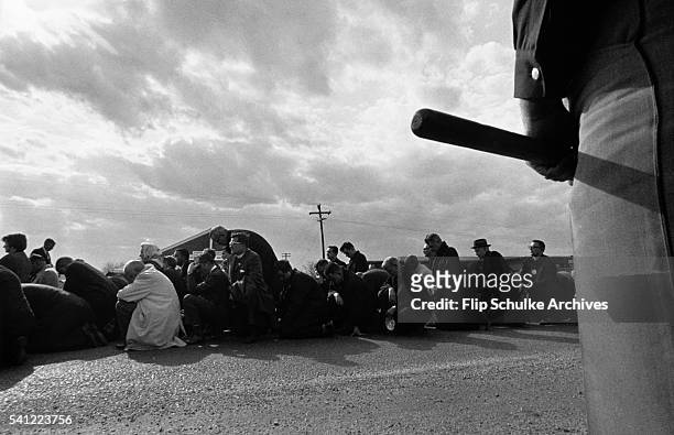 Large crowd of civil rights marchers kneel to pray after crossing the Edmund Pettus Bridge in Selma. A policeman stands nearby with his billy club...