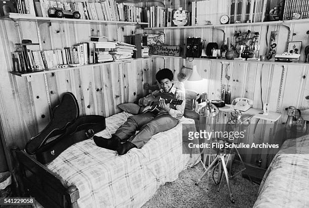 Dexter King, son of Martin Luther King Jr., plays a guitar while lounging in his bedroom.