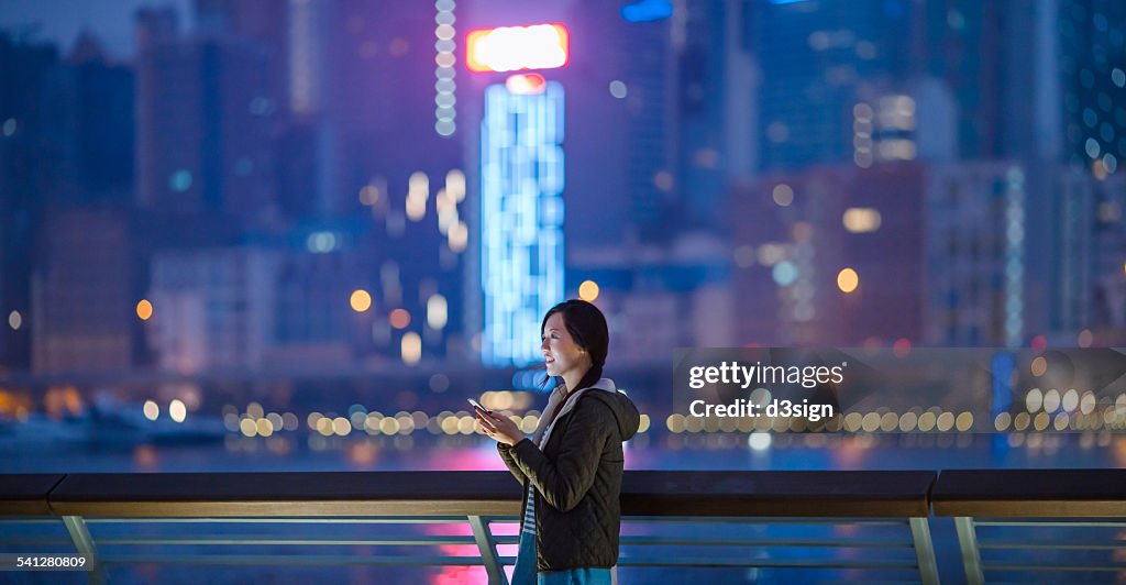 Joyful woman using smartphone in city looking away