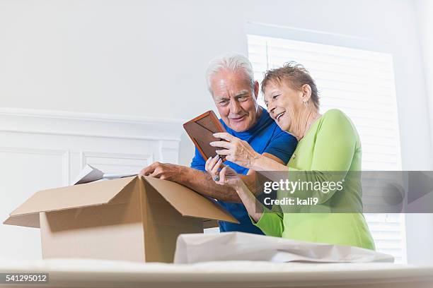 senior couple packing box, looking at picture frame - omstrukturering bildbanksfoton och bilder