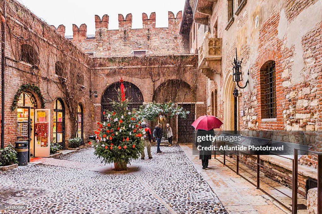 Casa di Giulietta (Juliet's house), a Christmas tree in the courtyard during a snowstorm, on the background the statue of Juliet and the famous balcony