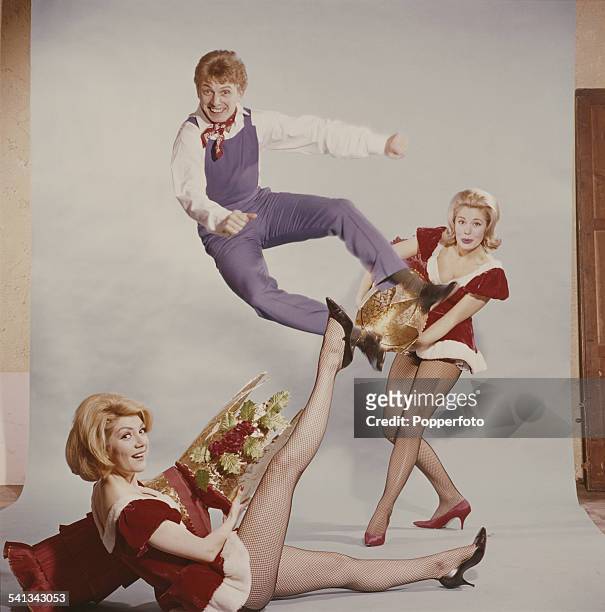 English entertainer Tommy Steele jumps out of an oversized christmas cracker pulled by two young women in festive costume in 1962.
