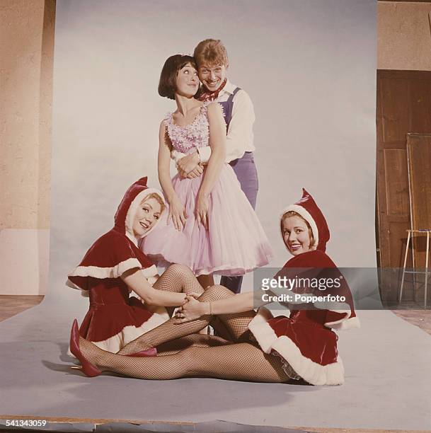 English entertainer Tommy Steele pictured with his arms around the waist of a young girl with two young women wearing festive costume sitting at...