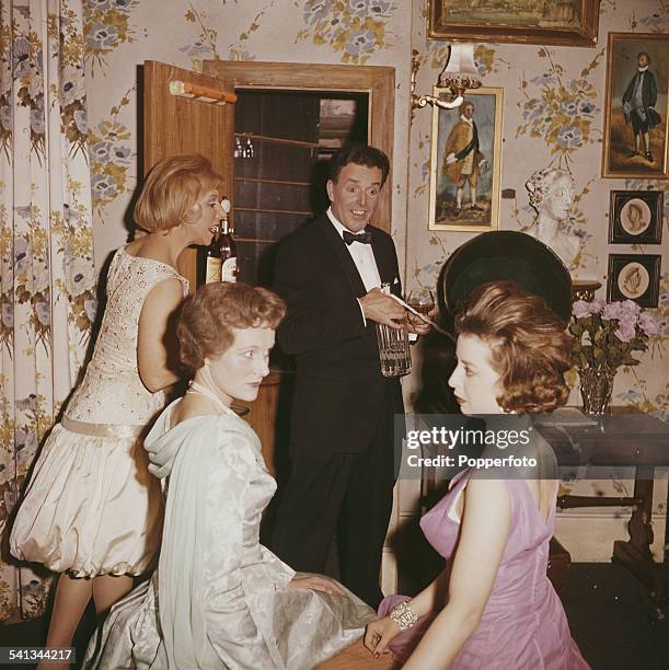 English actor Brian Rix pictured with three actresses, including Helen Jessop weaing a pink dress, in a scene from the play 'One for the Pot' in 1962.