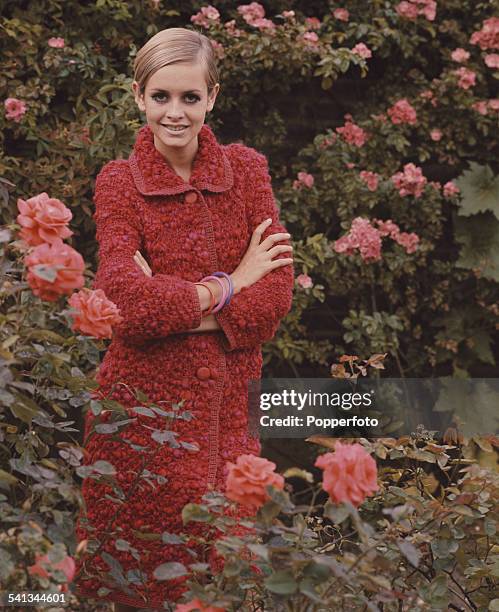 Sixties Fashion - English model Twiggy wears a red knee length woollen coat in a rose garden circa 1967.