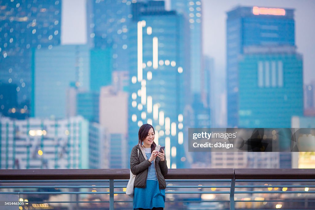 Woman smiling while using smartphone in city