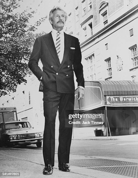 Low-angle portrait of American fashion designer Oleg Cassini stands on a street, 1955.