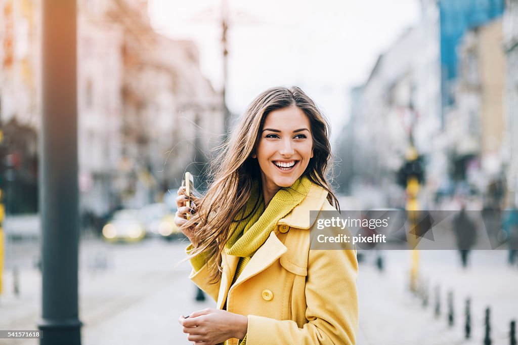 Smiling woman with a phone on the street