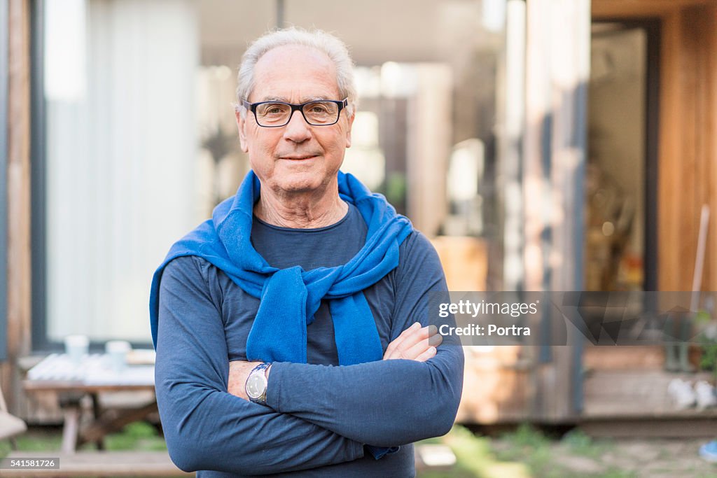 Confident senior man with arms crossed in backyard