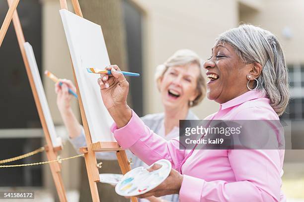 dos mujeres mayores divirtiéndose en clase de arte de pintura - leisure activity fotografías e imágenes de stock