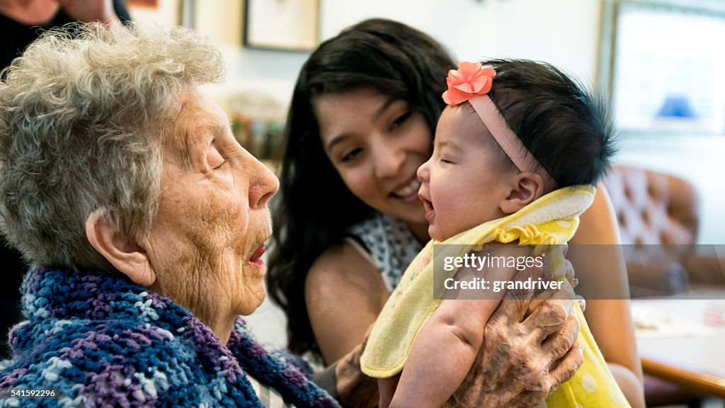 Elderly Woman Holding Infant Granddaughter as Mother Looks On Smiling