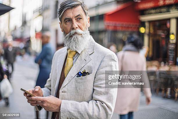 bearded mature man texting at the street - man baard stockfoto's en -beelden