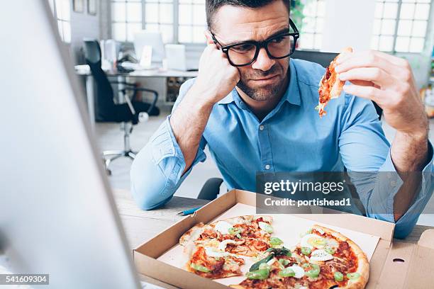 young businessman having unpleasent pizza lunch break at workplace - offensive stockfoto's en -beelden