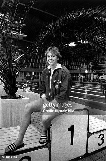 Sportlerin, Schwimmen DDR- sitzt in der DDR-Trainingsjacke auf demSiegerpodest mit Badelatschen- 1988