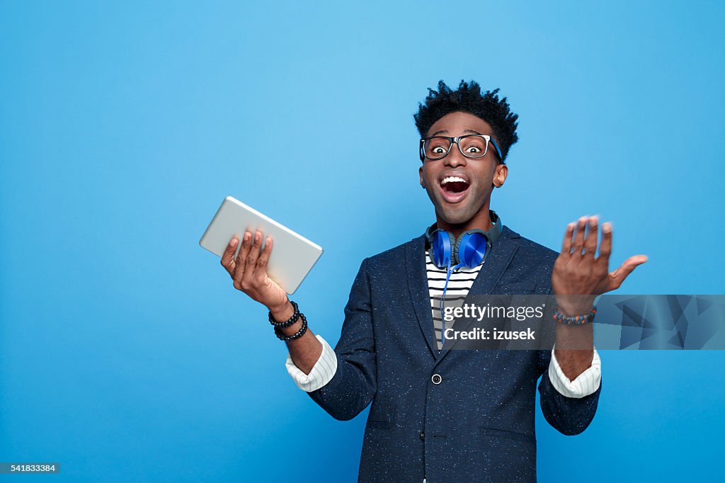 Excited afro american guy in fashionable outfit, holding digital tablet