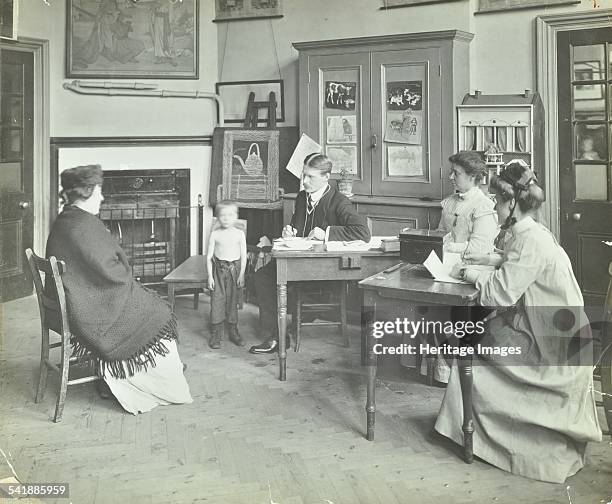 Medical examination of a boy, Holland Street School, London, 1911. A school doctor consulting a mother about her young son in the presence of two...