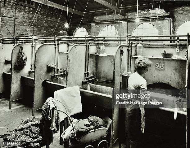 Boundary Street Area Laundry, Bethnal Green, London, 1964. A woman washes some clothes in a deep sink, while more clothes are piled on a pram behind...