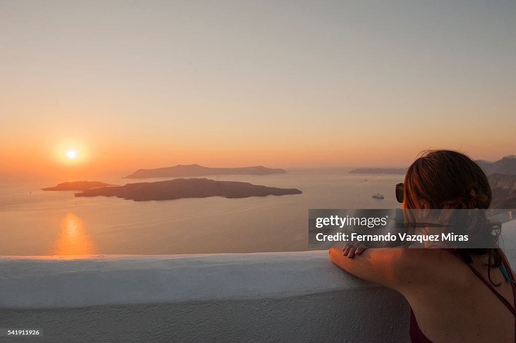 Woman observing an amazing Sunset in Santorini island, Cyclades islands, Greece