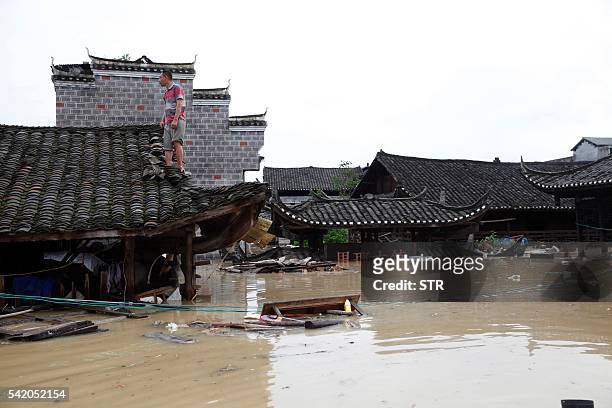 This photo taken on June 21, 2016 shows a man standing on the rood of a flood-inundated building in the flooded ancient town of Longshan county,...