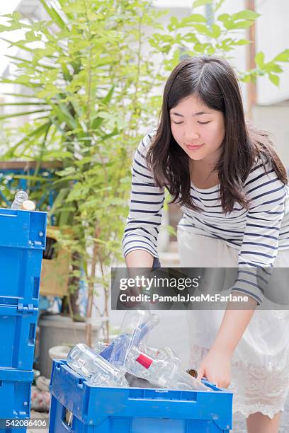 smiling young woman recycling glass bottles in alley, tokyo, japan - mixed recycling bin stock pictures, royalty-free photos & images